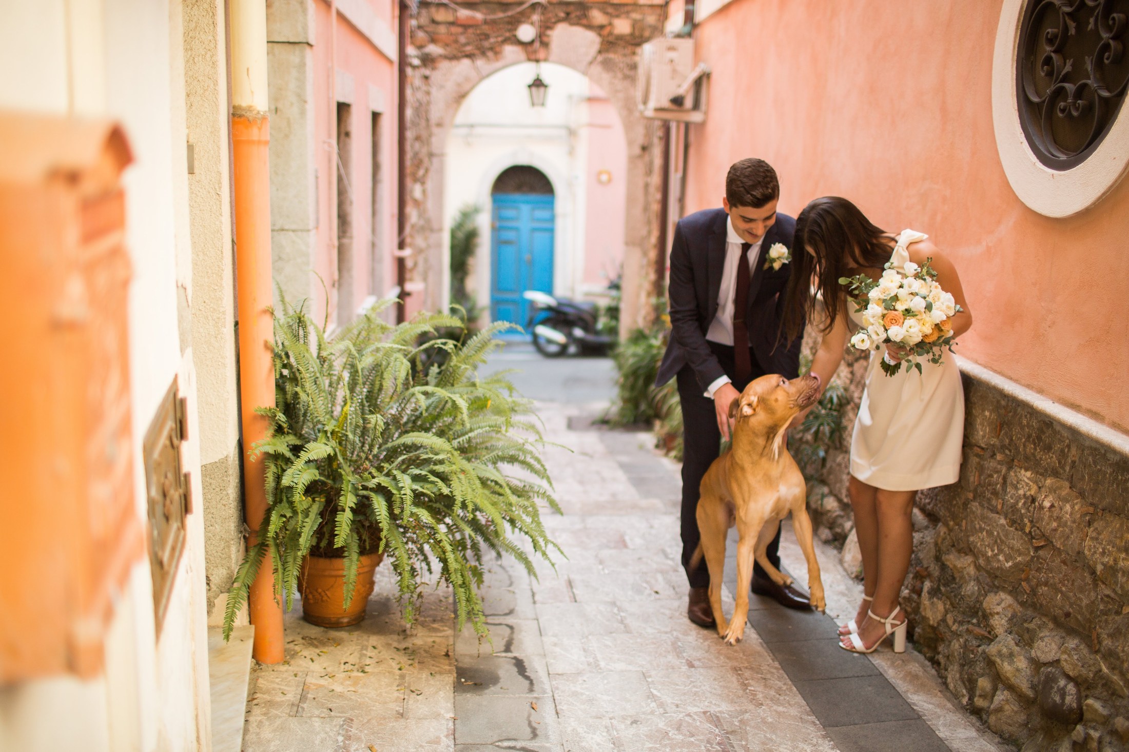 A couple on a Taormina terrace framed by bougainvillea, with the coastline and Mount Etna behind them