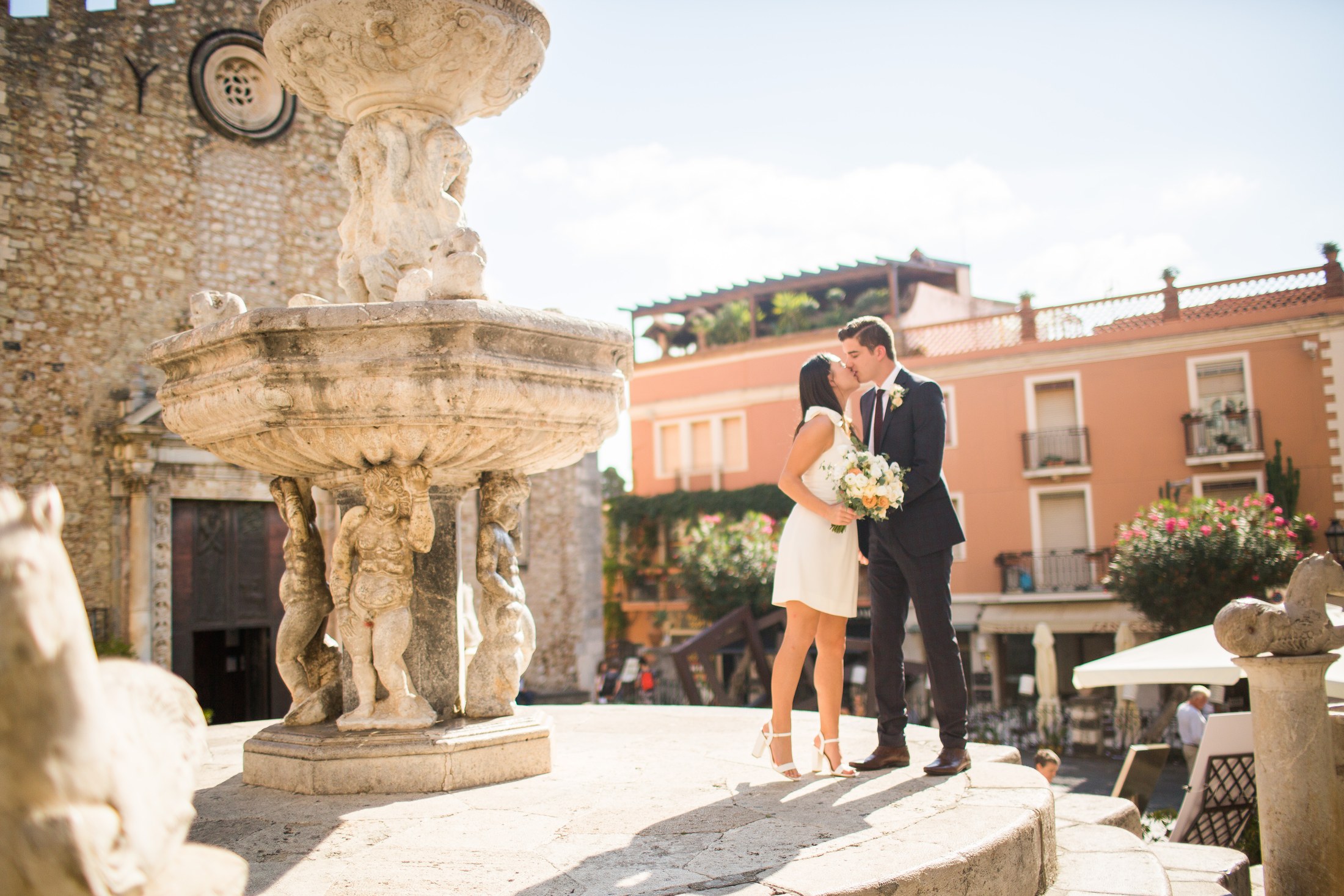 Michel and Heather laughing together during their civil ceremony inside Palazzo Duchi di Santo Stefano, framed by the palazzo’s weathered stone columns and rows of empty chairs behind them