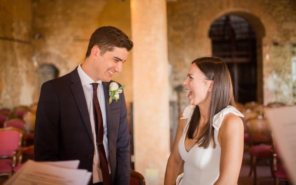 Michel and Heather sharing a kiss on the steps of an ornate carved stone fountain in a sunlit Taormina piazza, the bride holding a peach and white bouquet
