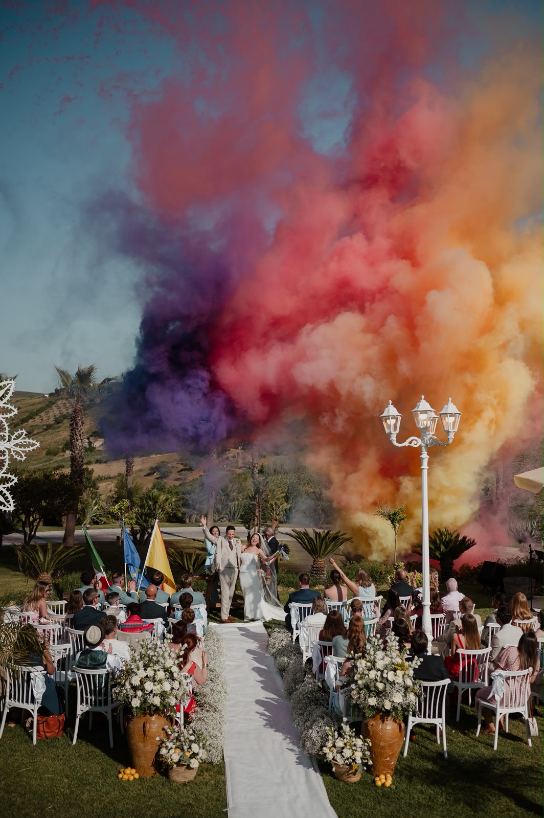 Jessica e Seb festeggiano lungo la navata avvolti da una nuvola di fumo colorato dopo la cerimonia