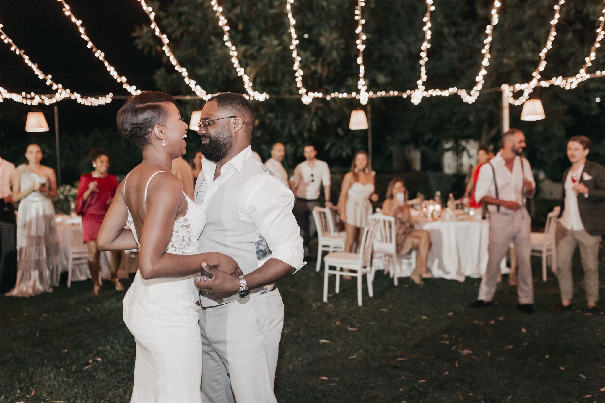 Kysha and Shem laughing together as they dance in the villa garden at night beneath strings of glowing fairy lights