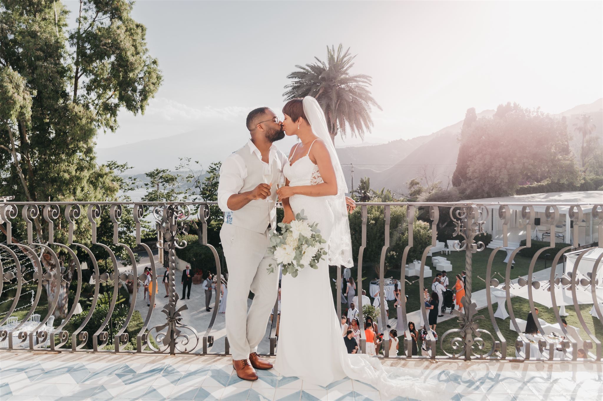 Kysha and Shem sharing a kiss on a Taormina terrace overlooking the sea and Mount Etna