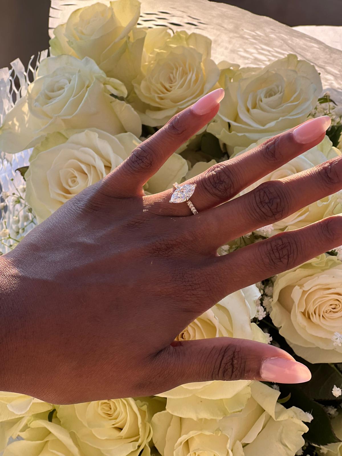 Close-up of a marquise-cut diamond engagement ring resting on a hand above white roses at a Sicilian proposal