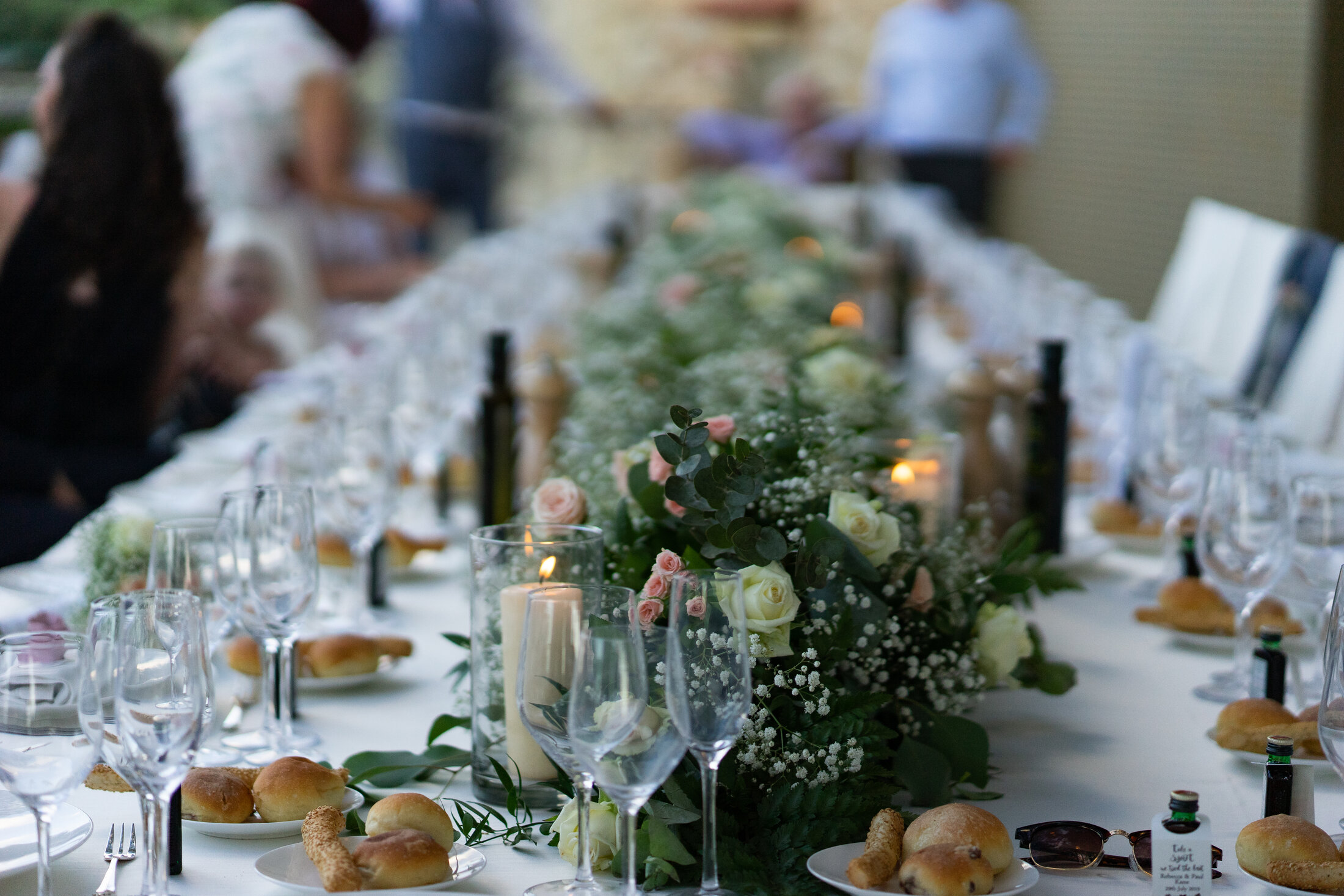 Long banquet table set for a Sicilian wedding reception with a lush floral runner of roses, gypsophila and eucalyptus, candles and fine glassware
