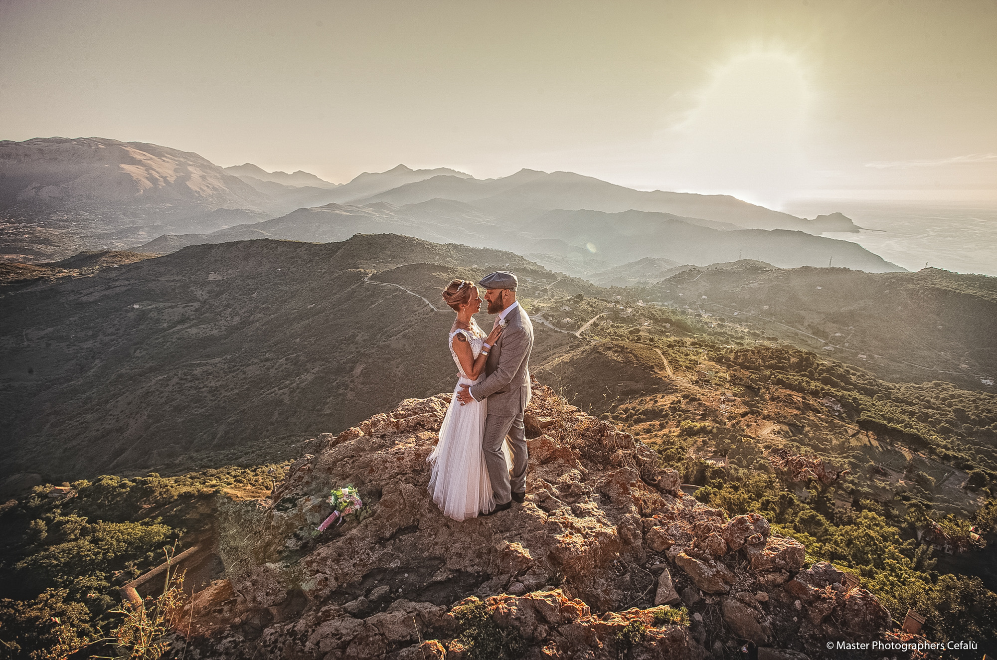 Real newlywed couple embracing on a Sicilian mountaintop at sunset overlooking the coast near Cefalu