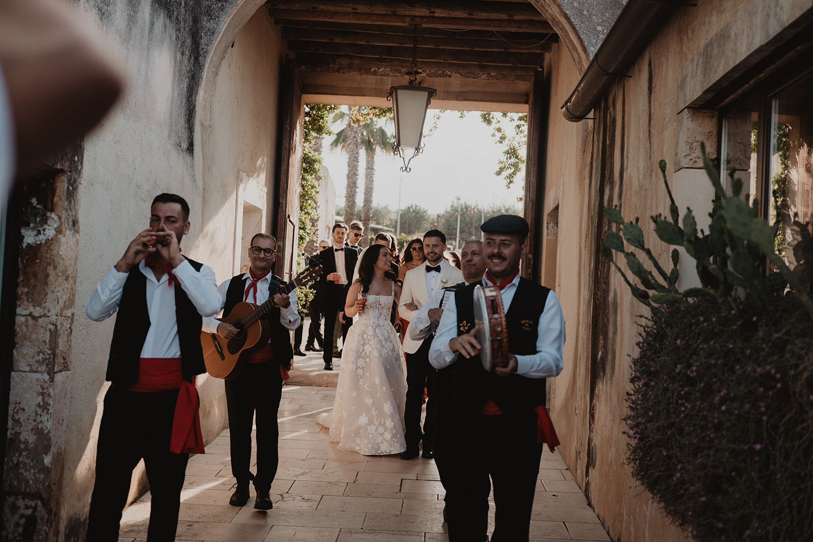 Musicisti folk siciliani guidano Lidia, Rian e i loro ospiti sotto un arco in pietra