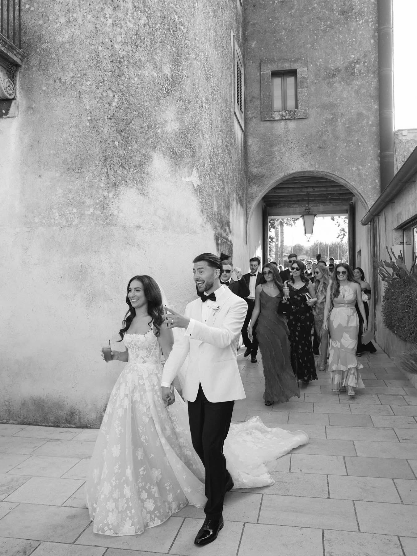 Una foto in bianco e nero di Lidia e Rian che attraversano il cortile con i loro ospiti