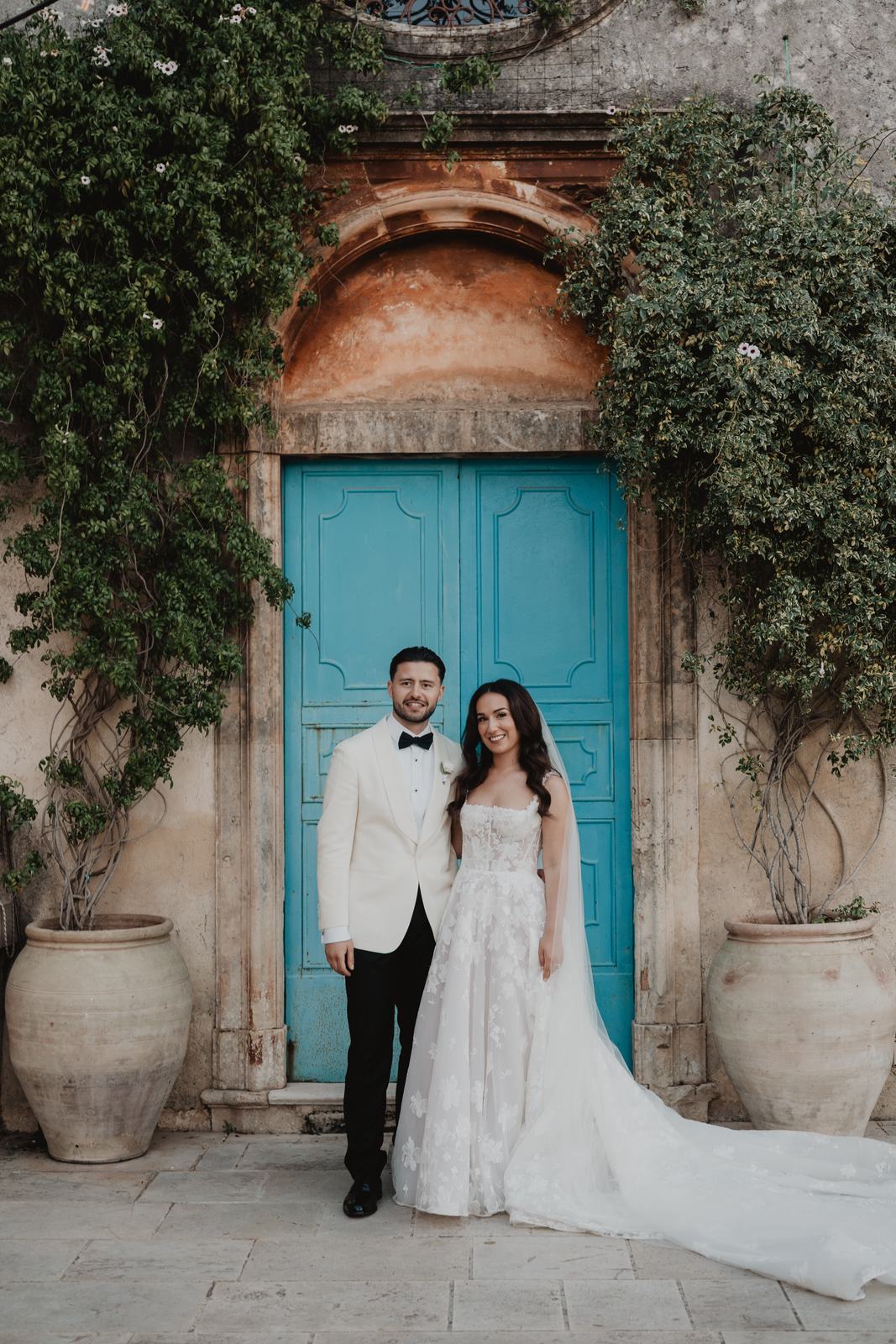 Gli sposi accanto a una porta azzurra incorniciata dall’edera al Borgo del Carato, location di campagna in Sicilia