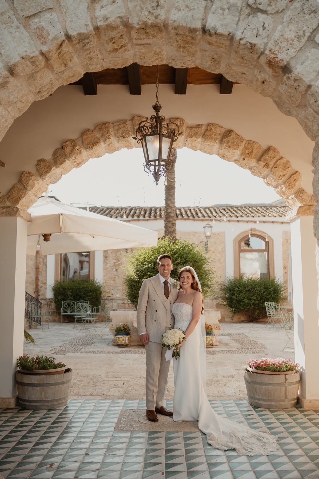 Gli sposi sotto l’arco in pietra del cortile in maiolica del Casale degli Aranci, location per matrimoni nella Sicilia occidentale