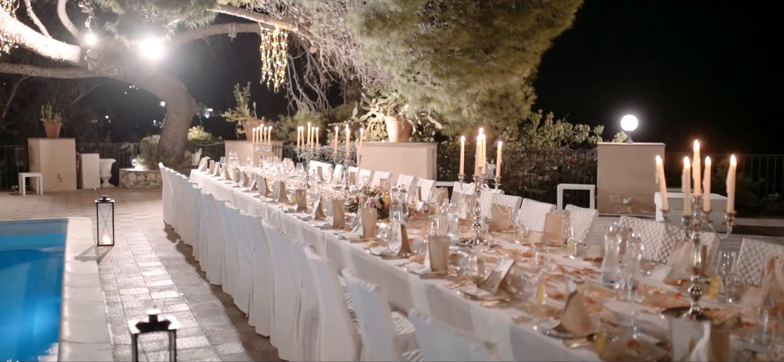 Una lunga tavolata nuziale a lume di candela accanto alla piscina nel parco dell’Excelsior Palace, Taormina